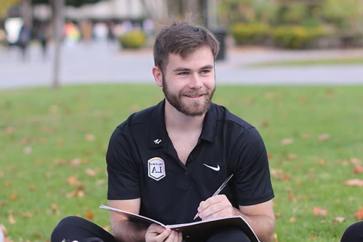 Student holding notebook and pen sitting on lawn